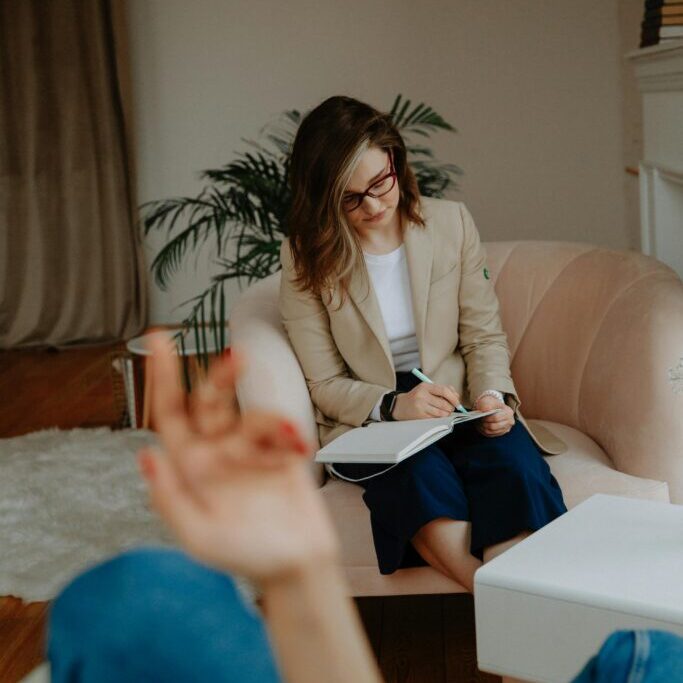 A therapist in a modern office takes notes while listening to a client.